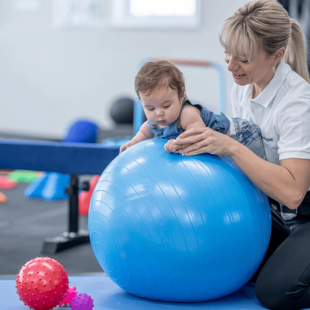 Infant receiving craniosacral therapy with therapist using a large blue ball.